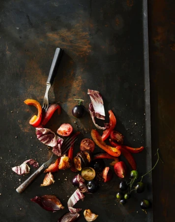 Overhead shot of red and purple vegetables on a dark, textured surface with a two-pronged fork, creating a vibrant and textured food composition.