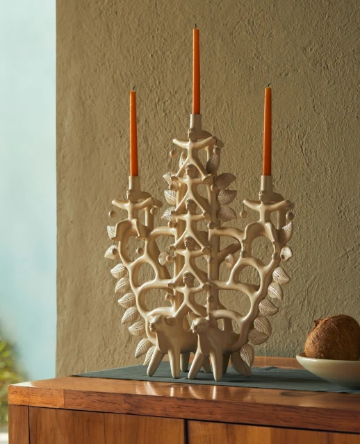 Ornate candelabra with three orange candles on a wooden cabinet against a textured wall, creating a warm and inviting atmosphere.