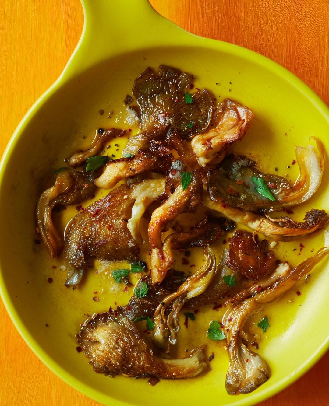 Overhead studio shot of sauteed mushrooms in a vibrant yellow bowl atop an orange surface, showcasing their rich color and texture.