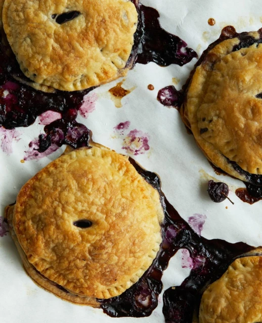 Overhead shot of freshly baked blueberry hand pies on parchment paper, showing golden crusts and oozing blueberry filling.