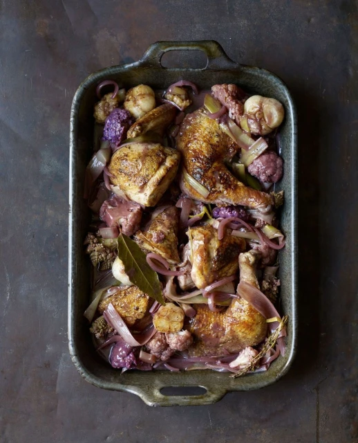 Overhead shot of roasted chicken pieces with vegetables, including onions and cauliflower, arranged in a dark metal baking pan.