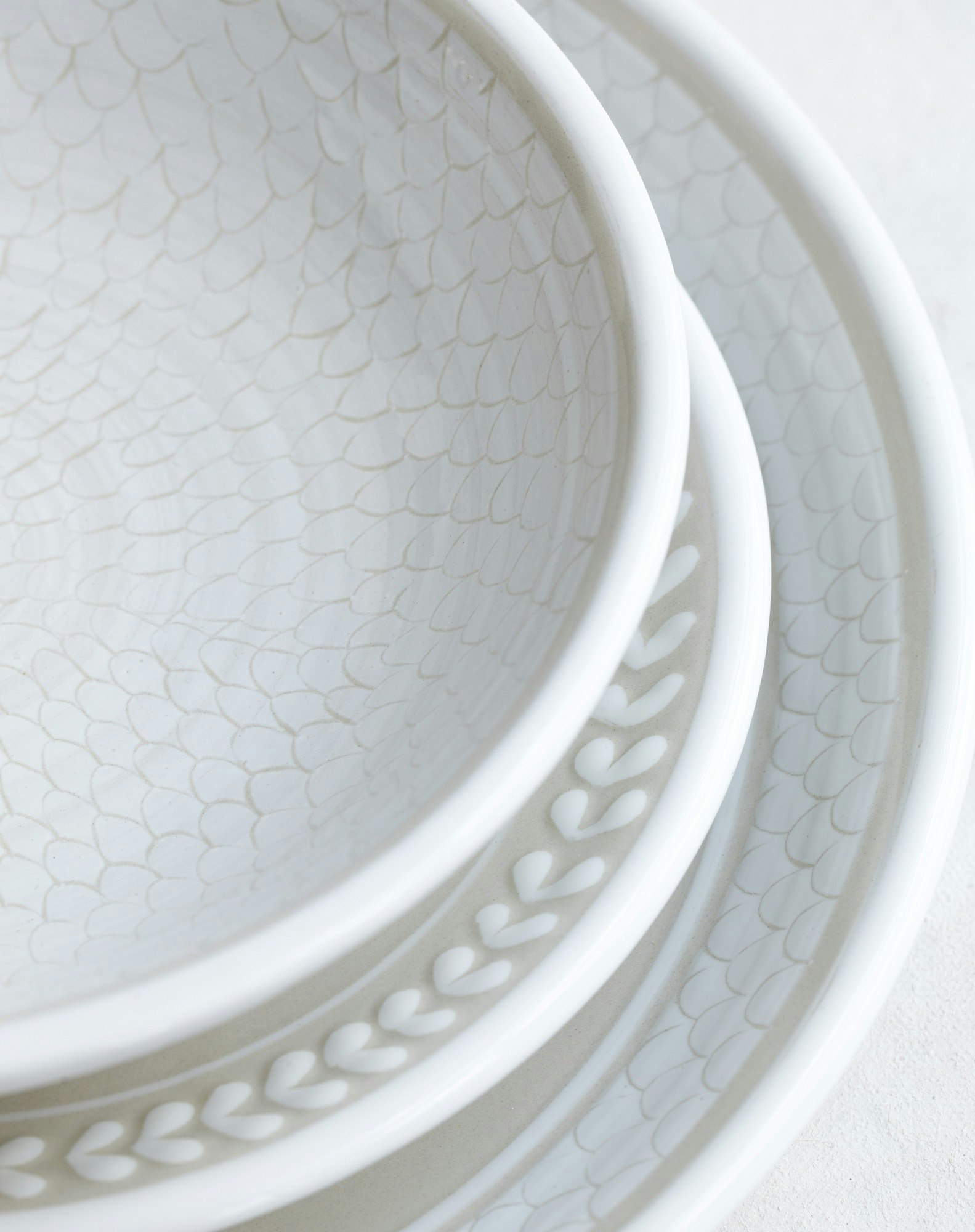 Close-up of stacked white ceramic tableware with leaf pattern rim and textured interior surface. Minimalist kitchenware product shot.