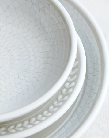 Close-up of stacked white ceramic tableware with leaf pattern rim and textured interior surface. Minimalist kitchenware product shot.