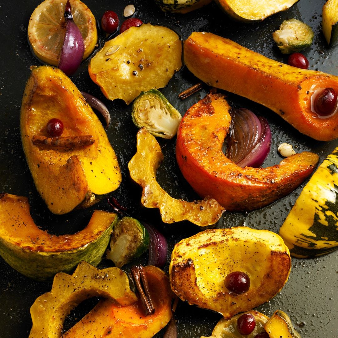 Overhead shot of roasted winter squash, Brussels sprouts, red onion, lemon slices, and cranberries on a black baking sheet. Food photography.