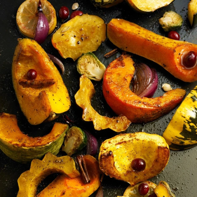 Overhead shot of roasted winter squash, Brussels sprouts, red onion, lemon slices, and cranberries on a black baking sheet. Food photography.