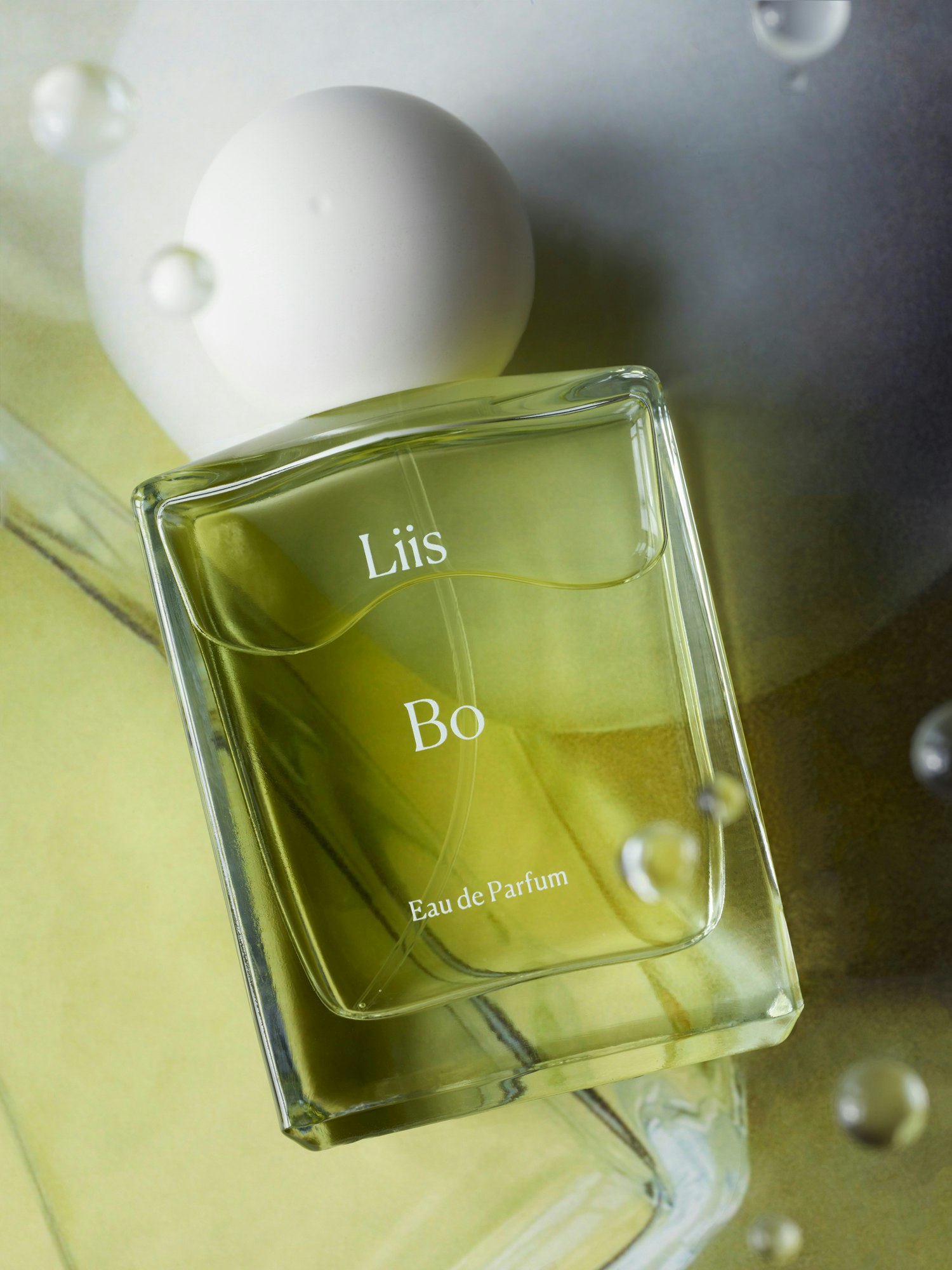 Overhead shot of a Liis Bo Eau de Parfum bottle with a white cap and spherical decorations against a light green background.