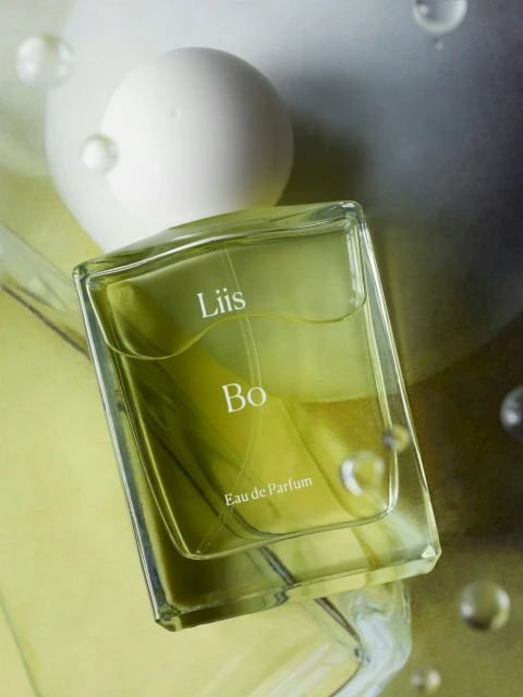 Overhead shot of a Liis Bo Eau de Parfum bottle with a white cap and spherical decorations against a light green background.