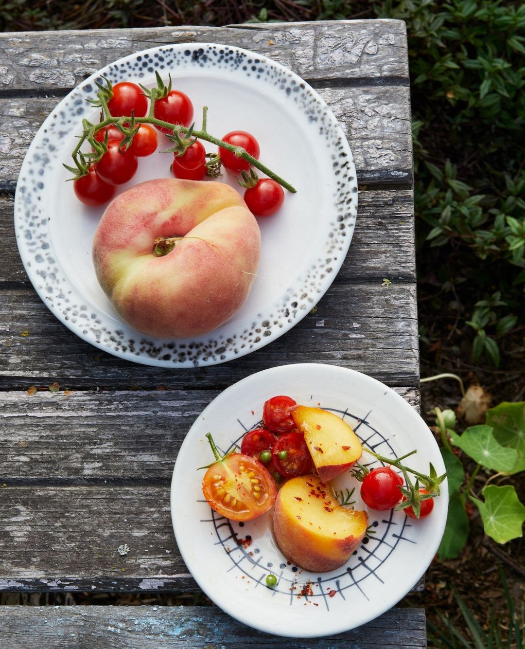 Overhead shot of a flat peach and cherry tomatoes on a white plate, with a second plate of sliced peach and tomatoes.