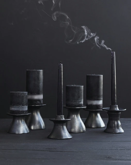 Still life of extinguished black candles in silver candle holders on a dark wooden surface with smoke rising in a dim setting.