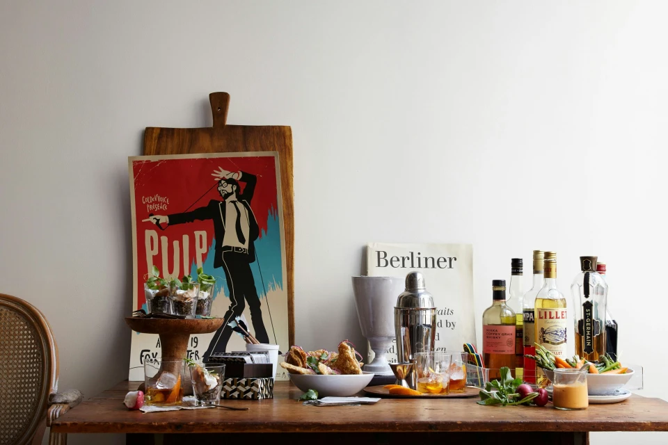 Still life on a wooden table: bottles, food, glasses, cocktail shaker, served with a Pulp Fiction movie poster on a wooden board.