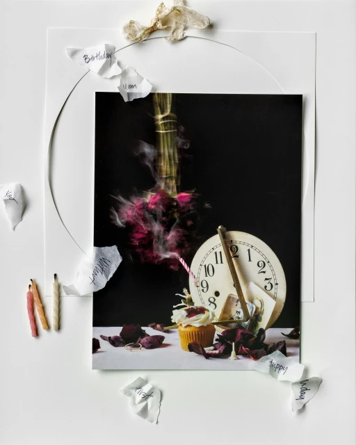 Still life photograph featuring a cupcake, an analog clock, a rose bouquet, and candle sticks surrounded by paper scraps with hand-written text.