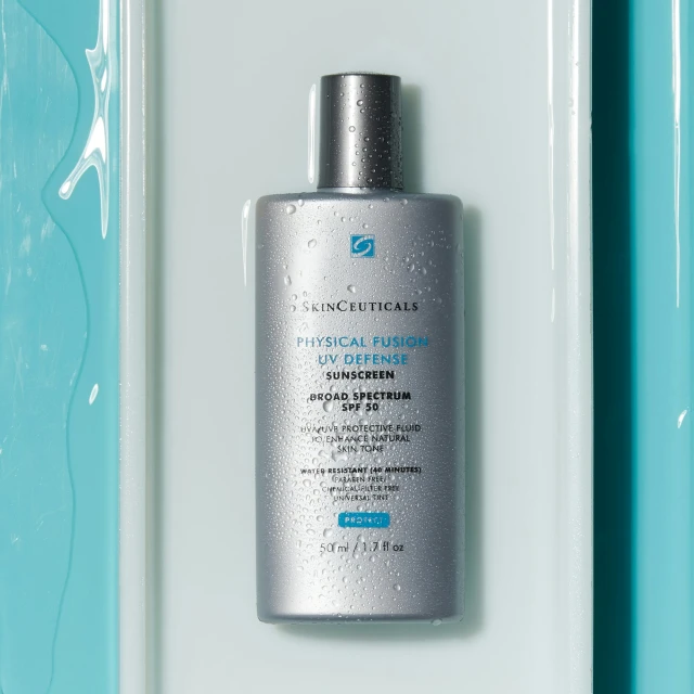 Silver bottle of SkinCeuticals Physical Fusion UV Defense sunscreen with water droplets against a light blue and white background.