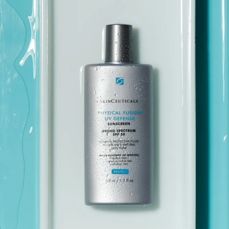 Silver bottle of SkinCeuticals Physical Fusion UV Defense sunscreen with water droplets against a light blue and white background.