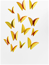 Overhead flat lay of several mango slices arranged into butterfly shapes on a white background, creating a whimsical food art design.