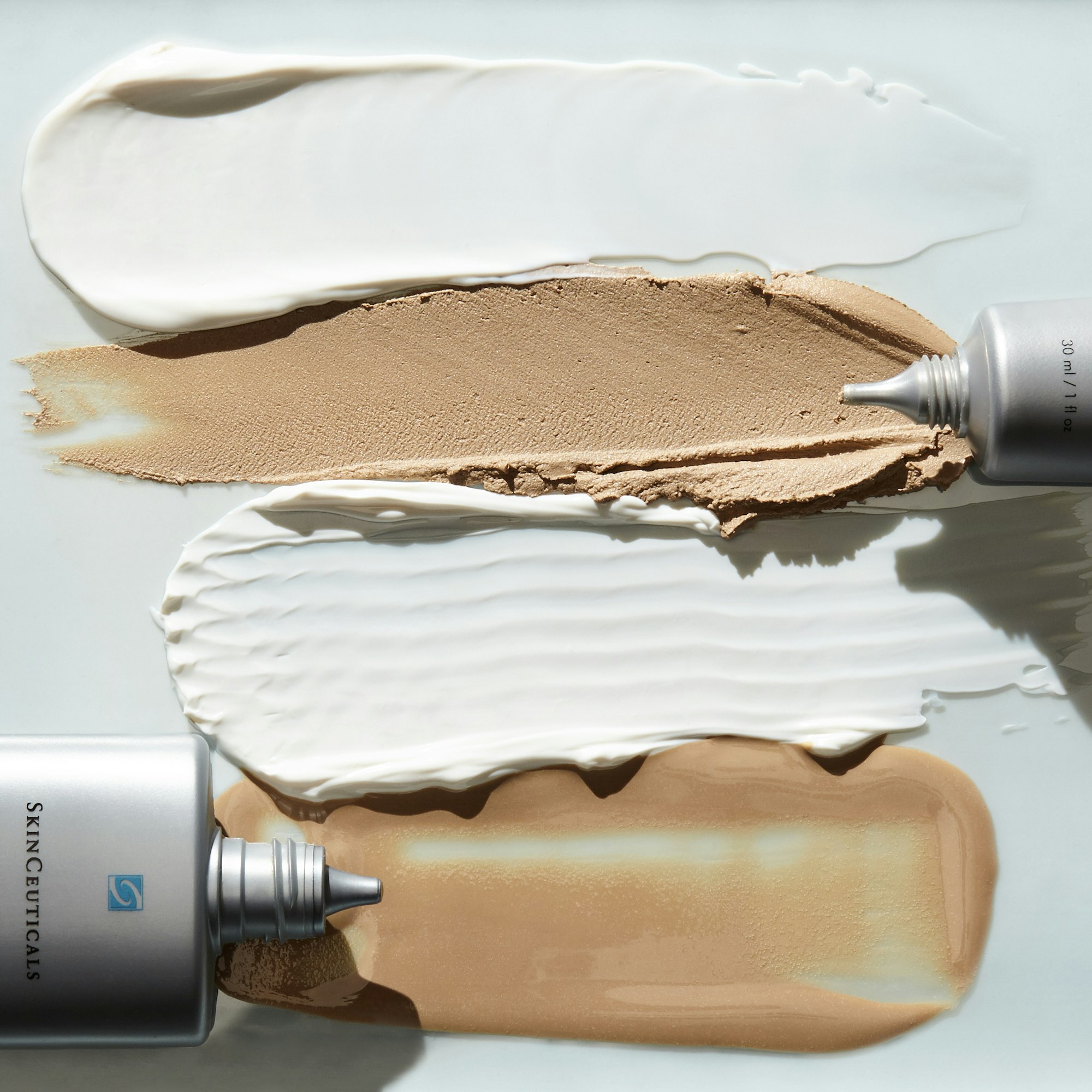 Close-up shot of Skinceuticals product tubes with cream swatches in white and tan on a light blue background for beauty concept.