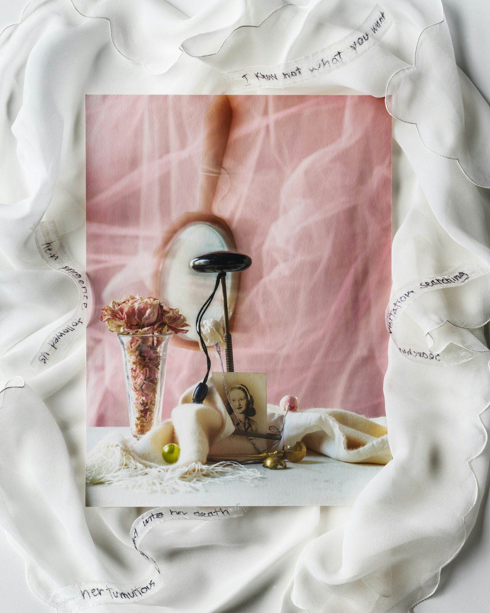 Still life of a vase with pink roses, jewelry, and a portrait photograph, styled with a semi-sheer white fabric with handwritten text.
