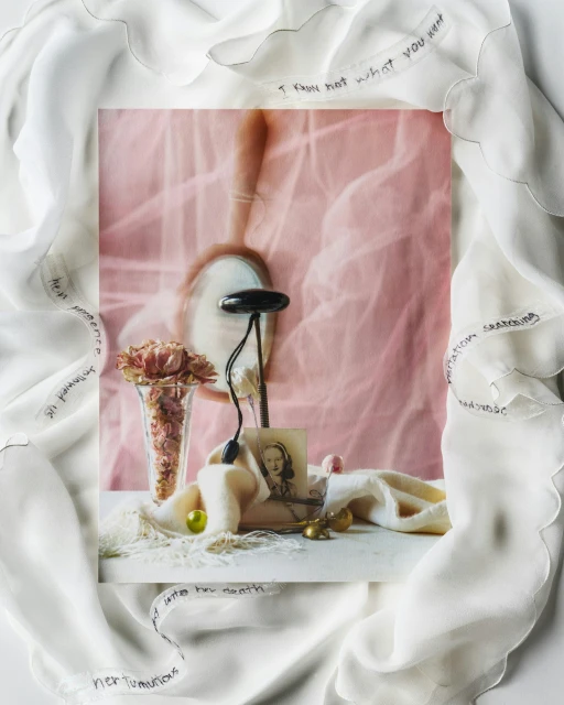 Still life of a vase with pink roses, jewelry, and a portrait photograph, styled with a semi-sheer white fabric with handwritten text.