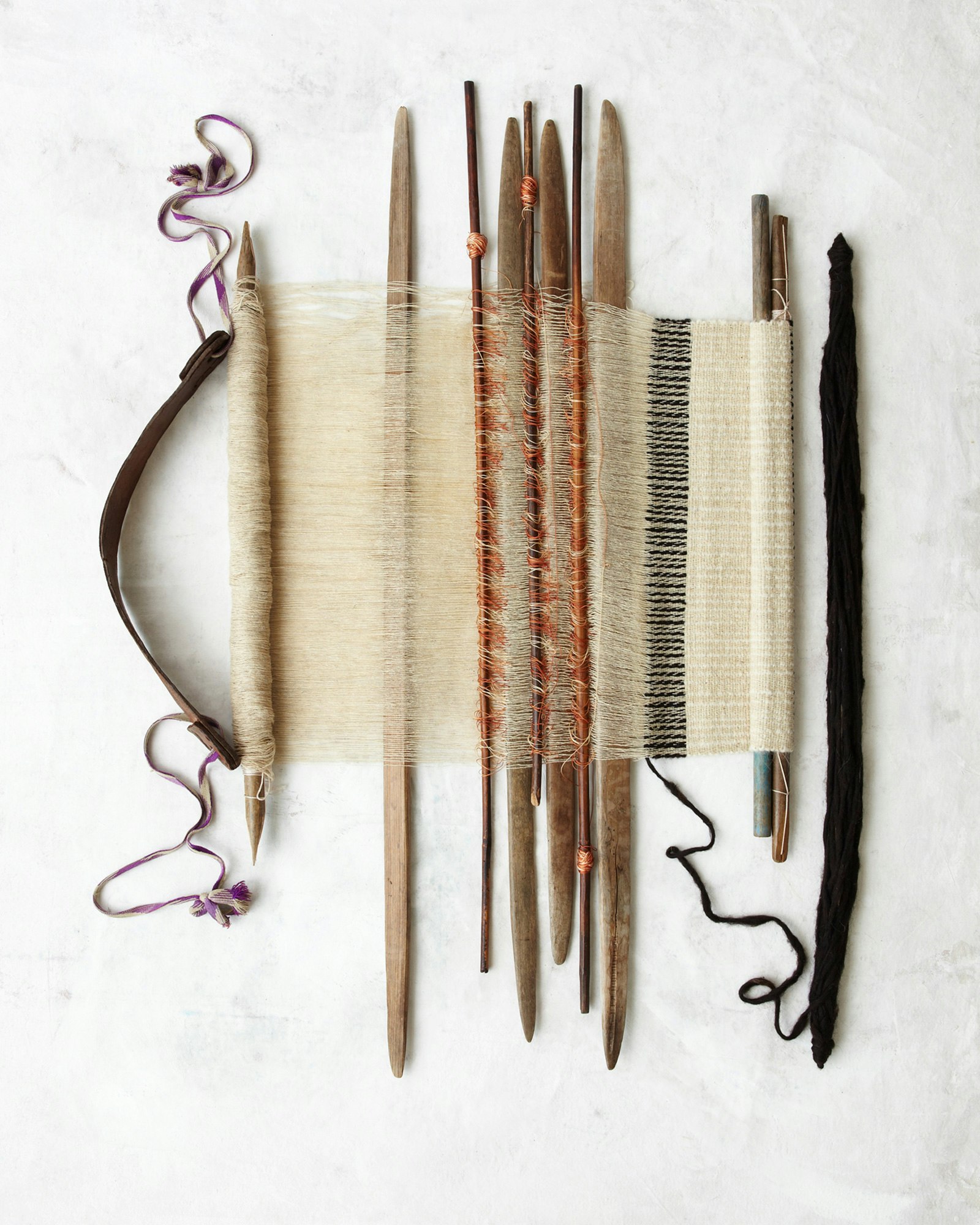 Overhead shot of a handloom with natural yarns, bobbins, and weaving tools on a textured white background, highlighting craftsmanship.