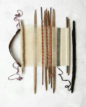 Overhead shot of a handloom with natural yarns, bobbins, and weaving tools on a textured white background, highlighting craftsmanship.