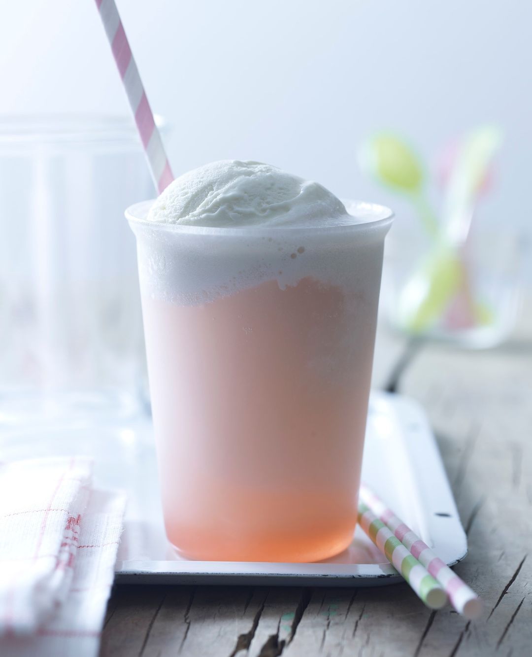 Iced drink with whipped topping and a pink striped straw on a light grey surface. Refreshing beverage with pale color palette.