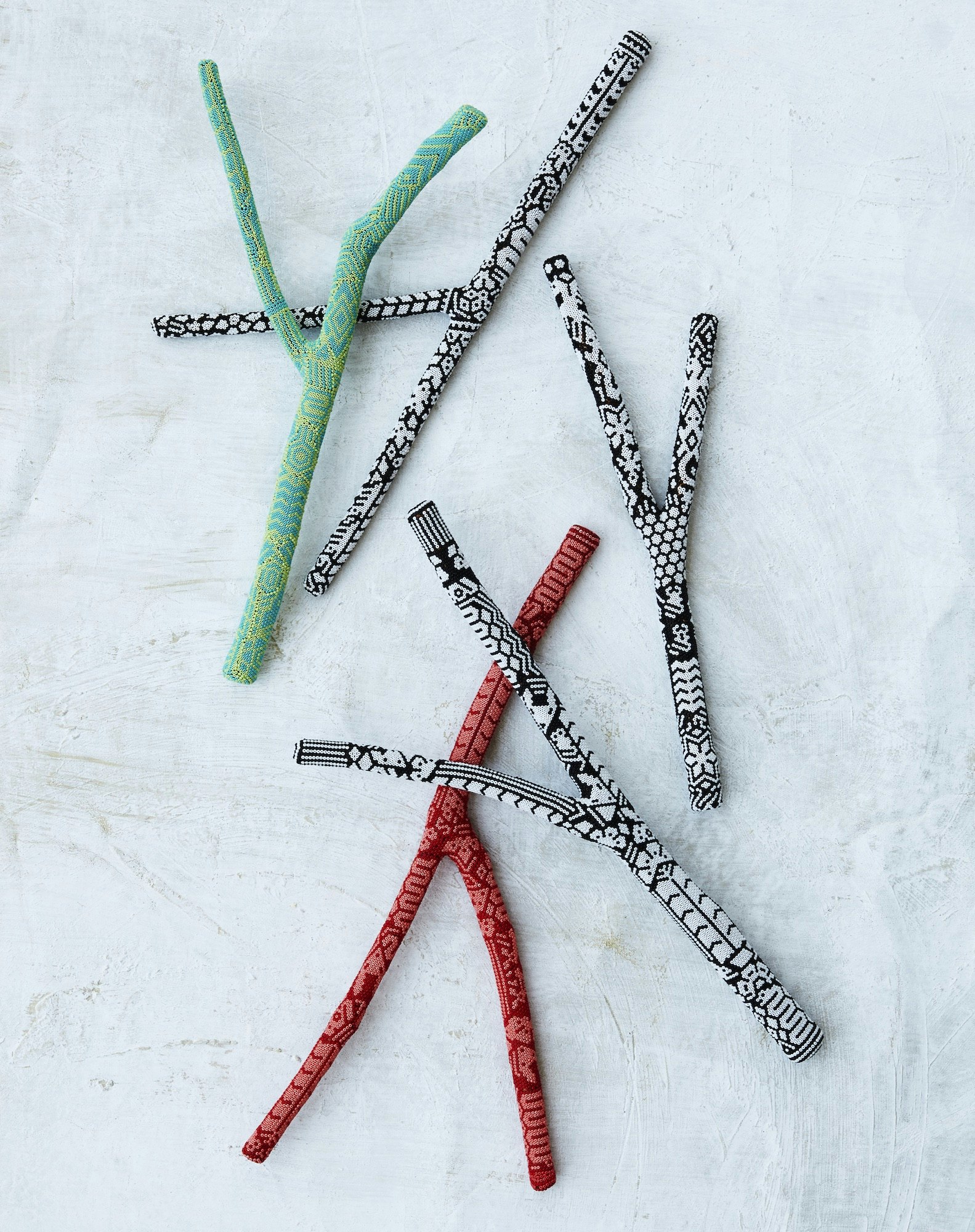 Overhead shot of several Y-shaped sticks with various black and white patterns and red and green colors scattered on a textured white surface.