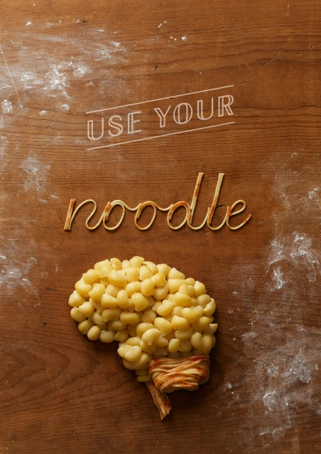 Overhead food shot of 'use your noodle' message made of pasta and gnocchi on a wooden surface with flour dust.