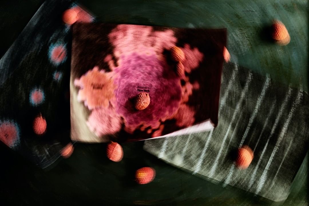 Abstract still life with lychees scattered around an album cover on a green surface, featuring blurred motion and vibrant pink and orange hues.