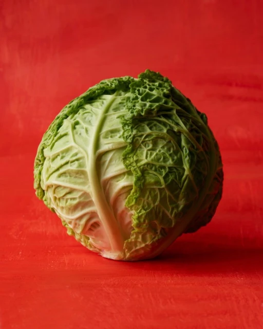 Studio shot of a vibrant green Savoy cabbage on a textured red surface, highlighting its ruffled leaves and fresh appearance.