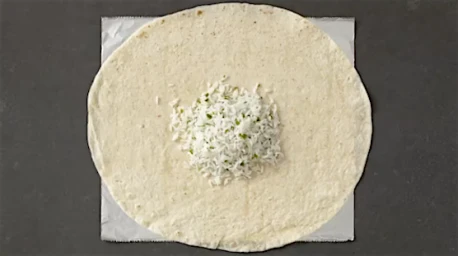 Top-down overhead view of a flour tortilla resting on foil with a mound of white rice in the centre.