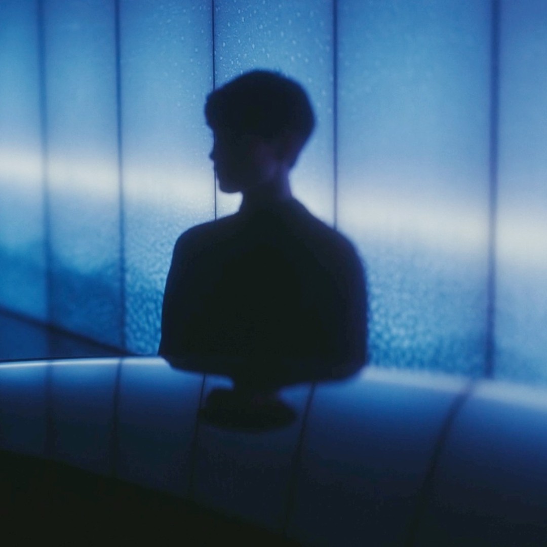 Silhouette of a person in a dark shirt against a textured blue wall with an illuminated line running horizontally through the middle.