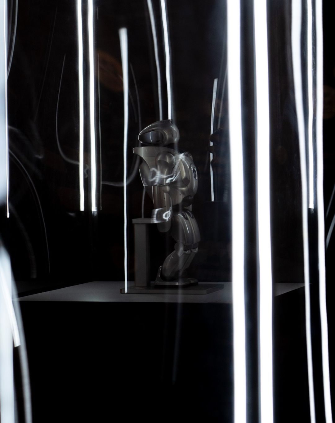 Abstract studio shot of a mannequin on a platform in front of a dark background with blurred streaks of white light. 