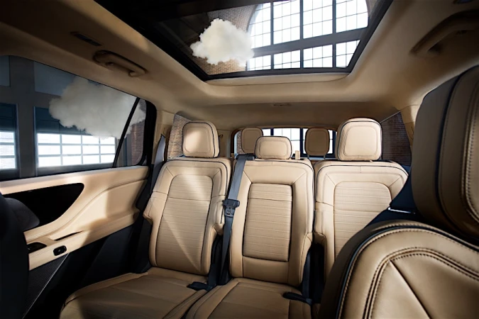 The interior of a luxury car showcases three rows of beige leather seats, a sunroof view with clouds, and modern automotive design.