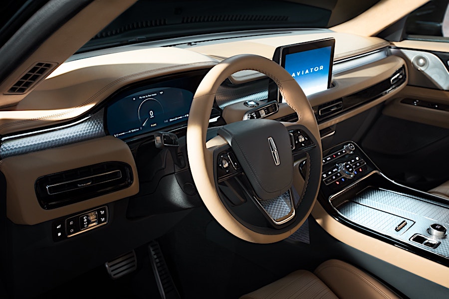 Tan interior of a Lincoln Aviator featuring a steering wheel with the logo, digital dashboard, and infotainment system display.