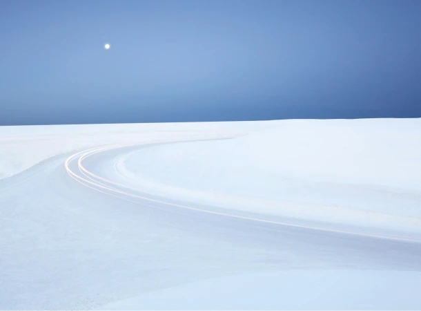 Snowy landscape with curving road and moonlight. Long exposure photography of light trails in a serene, minimal outdoor setting.