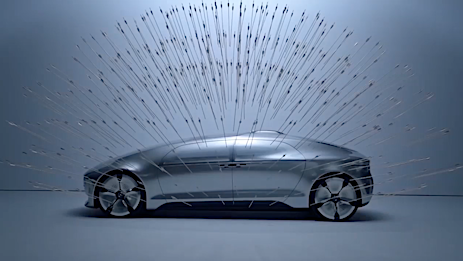 Sleek silver car in a wind tunnel simulation with air streams visualized over its surface, showcasing aerodynamic design.
