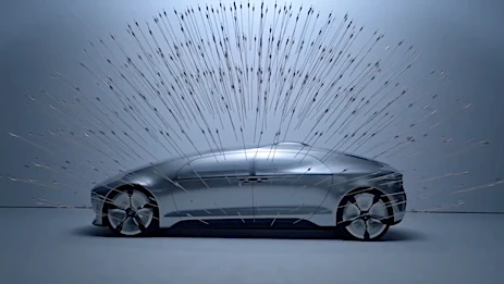 Sleek silver car in a wind tunnel simulation with air streams visualized over its surface, showcasing aerodynamic design.