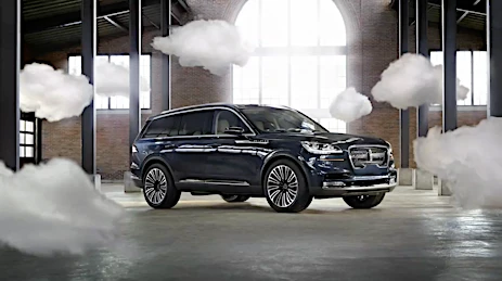 Dark blue luxury SUV parked in a brick warehouse interior with floating artificial white clouds around it.