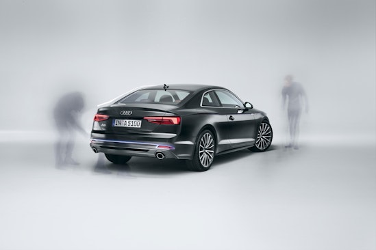 Sleek black Audi A5 coupe studio shot with stylized ghosting figures near the vehicle, promoting automotive design and technology.