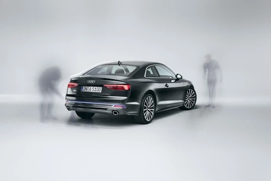 Sleek black Audi A5 coupe studio shot with stylized ghosting figures near the vehicle, promoting automotive design and technology.