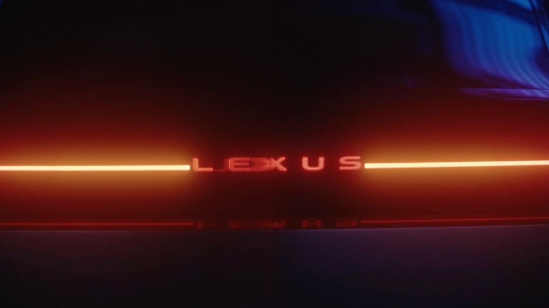 Close-up of a Lexus car taillight with illuminated red lettering on a dark background with blue light streak.