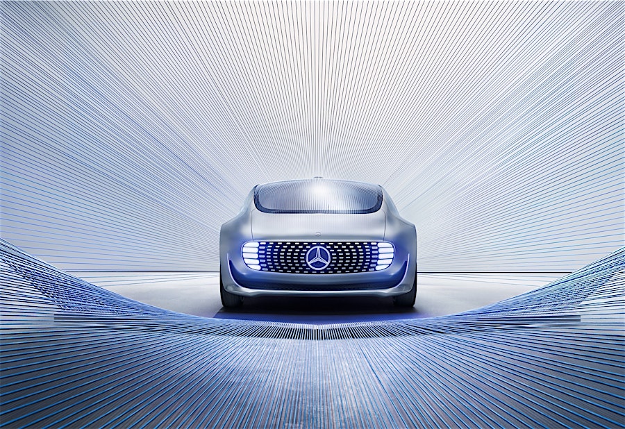 Silver Mercedes-Benz Vision AVTR concept car with blue illuminated grille, presented with blue light trails on a grey seamless background.