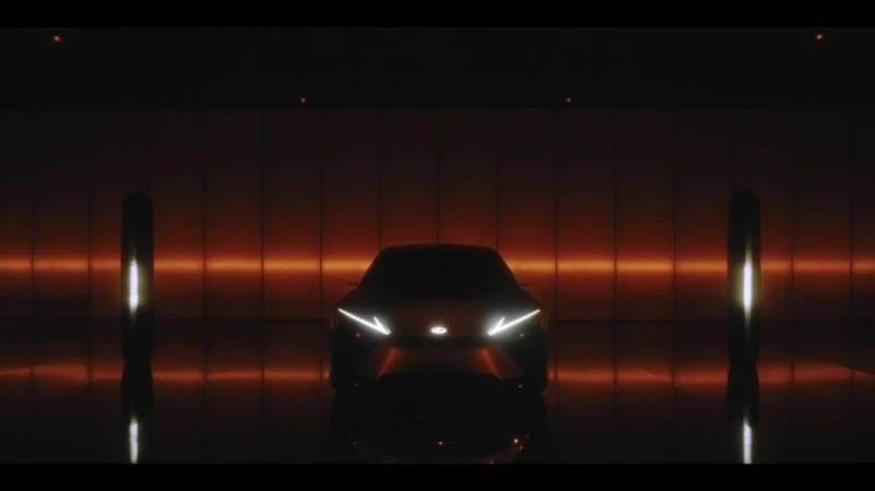 A dark automotive product shot of a car facing forward, with glowing headlights, in a dark photo studio with dark orange lighting.