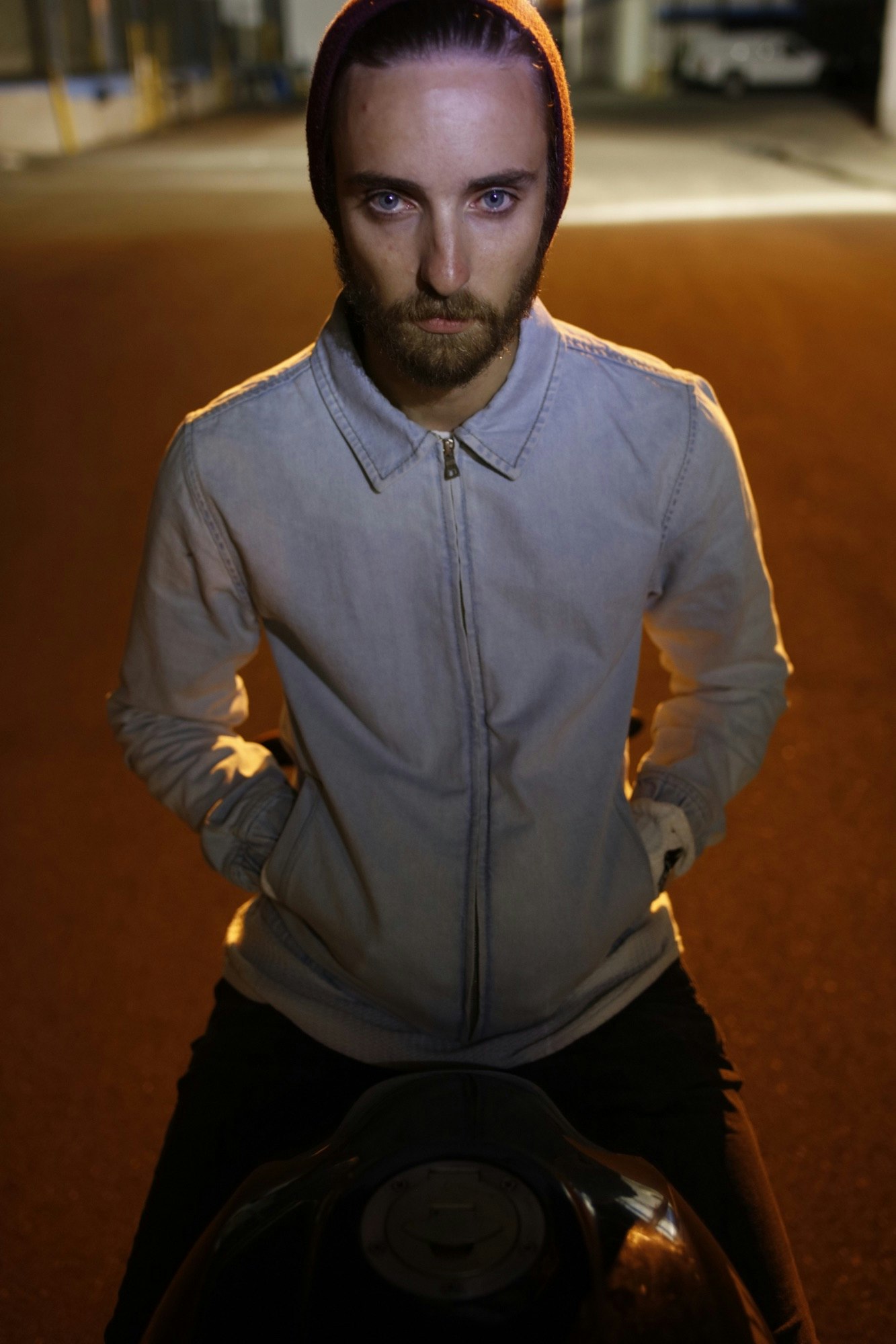 Man wearing a red beanie and light jacket seated on a motorcycle at night, photographed by Tobias Hutzler.