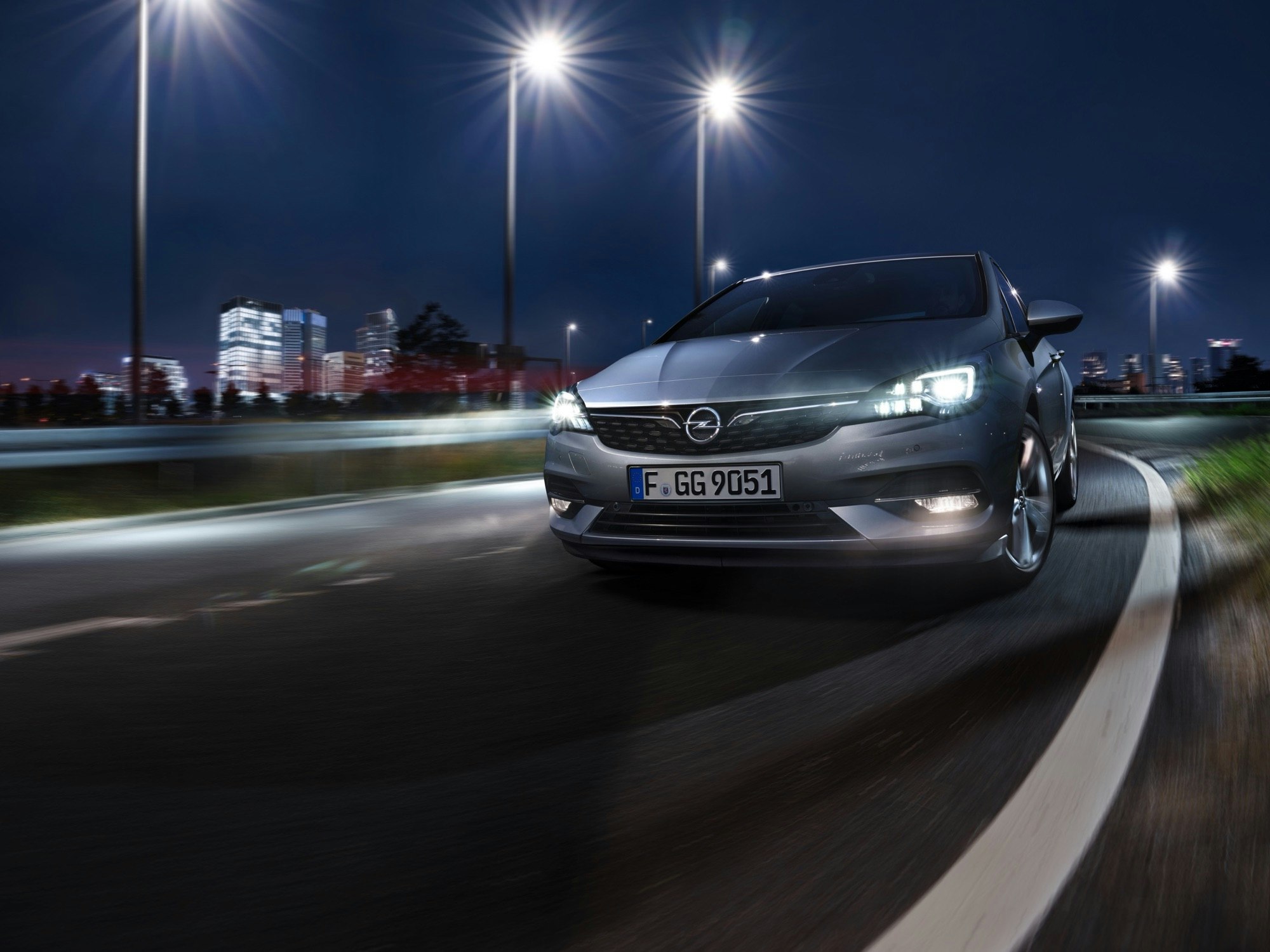 Sleek grey Opel Astra on a dark asphalt road at night with streetlights, creating a modern and dynamic automotive image.