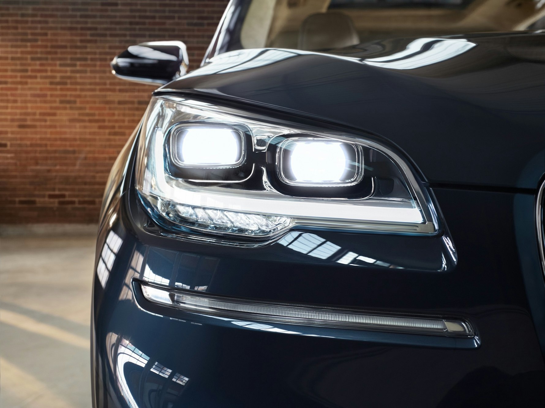Close-up of a dark blue car headlight against a blurred brick wall, showcasing modern automotive design and lighting technology.