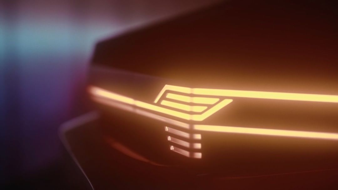 Close-up of a car's illuminated headlight with a geometric design, glowing a warm orange color in a dark environment.