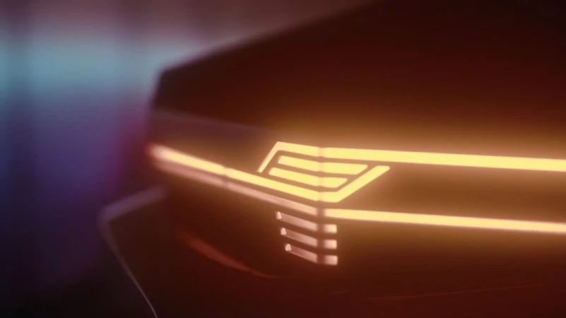Close-up of a car's illuminated headlight with a geometric design, glowing a warm orange color in a dark environment.