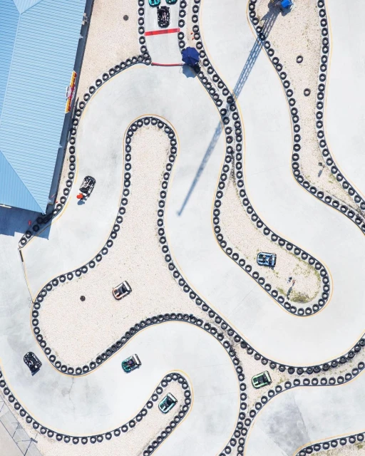 Aerial view of a go-kart track with several go-karts racing around a winding course lined with tires, creating a dynamic scene.