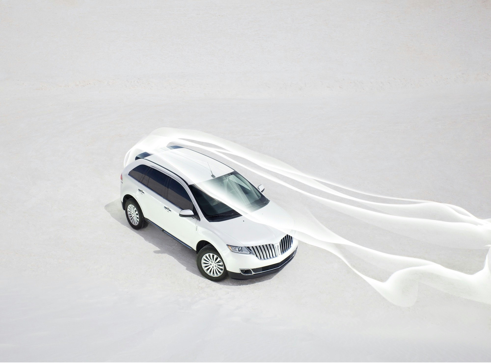 Aerial view of a white Lincoln SUV on a white surface, trailing white fabric, in bright daylight. Automotive and outdoor lifestyle imagery.
