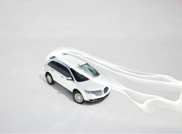 Aerial view of a white Lincoln SUV on a white surface, trailing white fabric, in bright daylight. Automotive and outdoor lifestyle imagery.